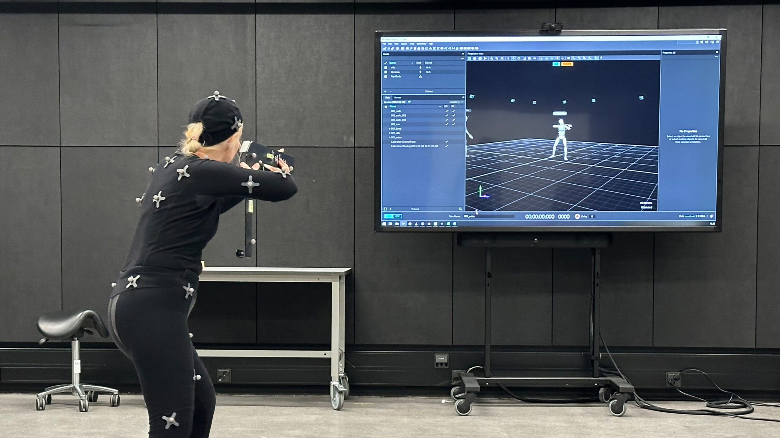 Liikkeenkaappauspukuun pukeutunut henkilö katsoo reaaliaikaista kuvaa itsestään television näytöltä. Henkilö on ampumisasennossa.