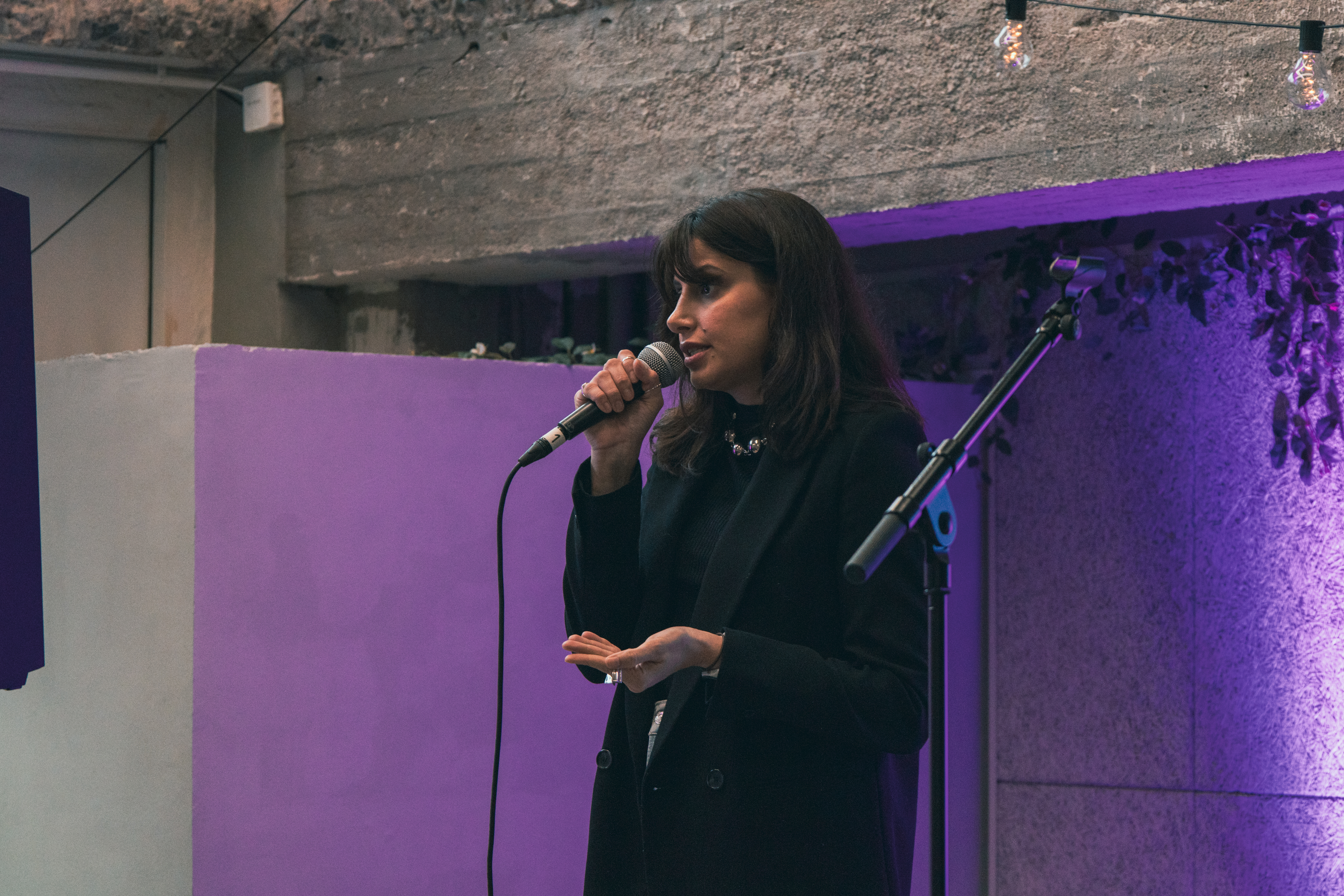 Marina Barboza standing on Monttu-stage in Metka Cafe, talking to the audience. She seems quite serious about the topic she's talking about.